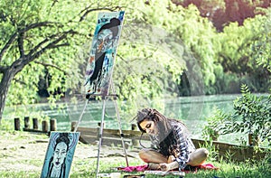 Young artist girl drawing draft in park near lake - Painter woman with dreadlocks hairstyle working on her art in the nature