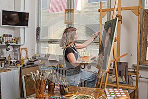 Young artist in his Studio painting a picture. Female hands of the young artist and oil paint