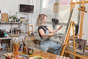 Young artist in his Studio painting a picture. Female hands of the young artist and oil paint