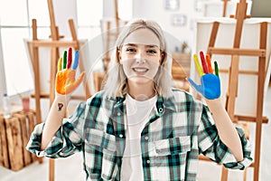 Young artist student girl smiling happy showing colorful painted hands at art studio