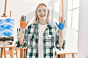 Young artist student girl smiling happy showing colorful painted hands at art studio