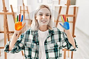 Young artist student girl smiling happy showing colorful painted hands at art studio