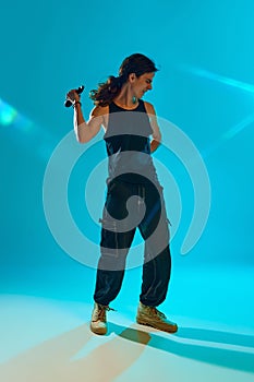 Young artistic man, musician raps with energy, singing against blue, cyan background in neon light. Entertainment event