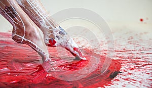 Young artistically abstract painted woman ballerina with black red white, paint, pokes her feet in red paint, Creative body art