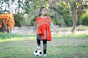 A young Asain girl playing football with her big black dog outside the grass ground in the yard in the evening