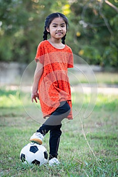 A young Asain girl playing football with her big black dog outside the grass ground in the yard in the evening