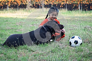 A young Asain girl playing football with her big black dog outside the grass ground in the yard in the evening