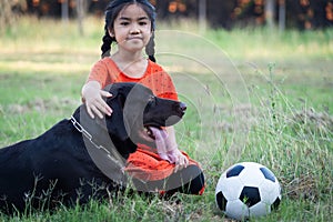 A young Asain girl playing football with her big black dog outside the grass ground in the yard in the evening