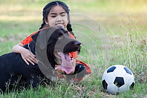 A young Asain girl playing football with her big black dog outside the grass ground in the yard in the evening