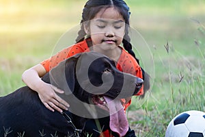 A young Asain girl playing football with her big black dog outside the grass ground in the yard in the evening