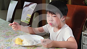 Young Asia boy in white T-shirt having omelet in the morning at table in the living room