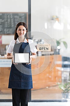 Young asia business owner woman with apron with open sign at cafe open again, showing blank white screen of tablet.