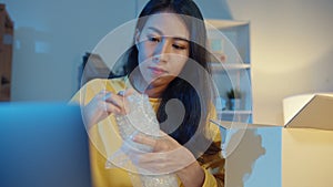 Young Asia businesswoman packing glass use bubble wrap for packing support damage fragile product in home office at night. Small