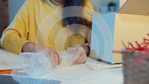 Young Asia businesswoman packing glass use bubble wrap for packing support damage fragile product in home office at night. Small