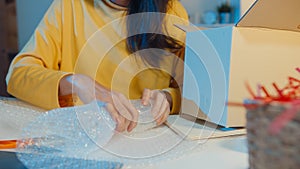 Young Asia businesswoman packing glass use bubble wrap for packing support damage fragile product in home office at night. Small