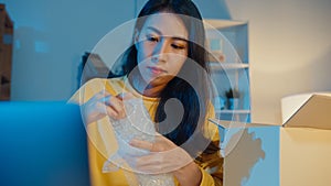 Young Asia businesswoman packing glass use bubble wrap for packing support damage fragile product in home office at night. Small