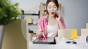 Young Asia businesswoman using mobile phone call receiving purchase order and check product on stock, work at home office. Small