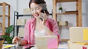 Young Asia businesswoman using mobile phone call receiving purchase order and check product on stock, work at home office. Small