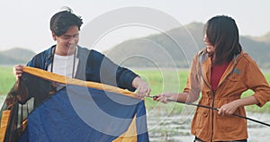 Young asia campers couple setting up the tent camping gear outdoor near seaside. Male and female travel having fun on a summer day