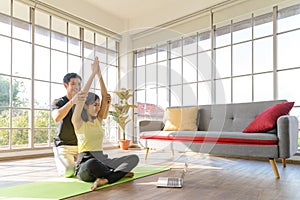 Young Asia couple practicing yoga lesson, breathing, meditating together and watching videos on laptop in living room at home. hea
