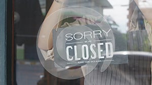 Young Asia girl wear face mask turning a sign from closed to open sign on door looking outside waiting for clients after lockdown