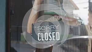 Young Asia girl wear face mask turning a sign from closed to open sign on door looking outside waiting for clients after lockdown