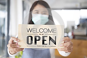 Young Asia girl wear face mask turning a sign from closed to open sign after lockdown