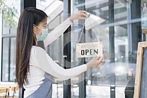 Young Asia girl wear face mask turning a sign from closed to open sign after lockdown