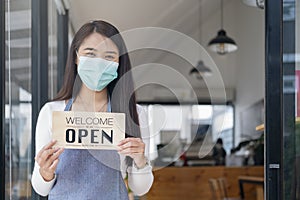 Young Asia girl wear face mask turning a sign from closed to open sign after lockdown.