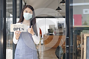 Young Asia girl wear face mask turning a sign from closed to open sign after lockdown.