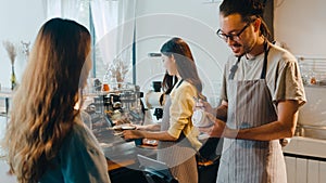 Young Asia male barista waiter taking order from customer standing behind bar counter while talking with customer making note on