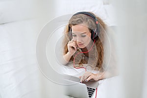 Young Asia man relaxing on the bed, listening to music with headphones and and using laptop