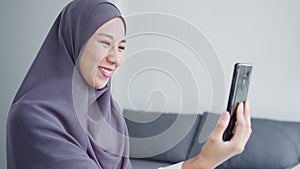 Young Asia muslim businesswoman using smart phone talk to friend by videochat brainstorm online meeting while remotely work from
