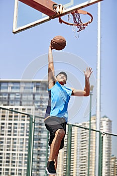 Young asian adult man dunking basketball