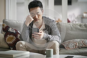 young asian adult man looking at cellphone at home