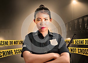 Young Asian American police officer standing serious in custody of crime scene for preserving evidence at do not cross police line