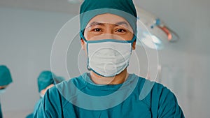Young Asian assistants man looking at camera and smiling after performing invasive surgery on patient in hospital operating room.