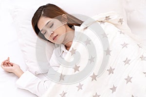 Young asian attractive woman sleeping in soft white pillow and bed on top view with white shirt pajamas and stars blanket.