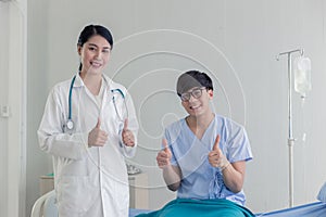 Young Asian beautiful doctor and Asian teenage patient showing thumbs up with smiley face in the hospital