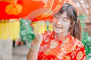 Young asian beautiful girl in chinese traditional red dress smile stand near china lamp, in the Chinese New Year. Festivities.