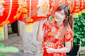Young asian beautiful girl in chinese traditional red dress smile stand near china lamp, in the Chinese New Year. Festivities.