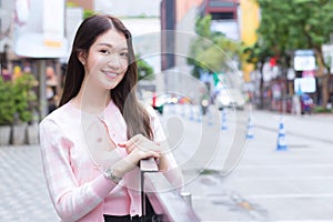 Young Asian beautiful woman in a pink and white striped coat is smile standing urban outdoors with the city and road as a