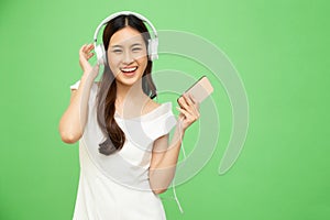 Young Asian beauty woman dancing and listening music with headphones on smartphone isolated on green background.