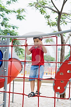 Young asian boy climb on the red rope fence and gray bar by his