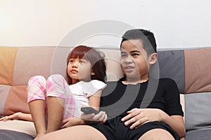 Young Asian boy and girl sibling sitting on the couch and watching tv