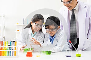 Young Asian boy and girl student wearing protective google while study and do science experiment in classroom with teacher.