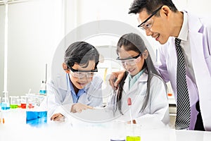 Young Asian boy and girl student wearing protective google while study and do science experiment in classroom with teacher.