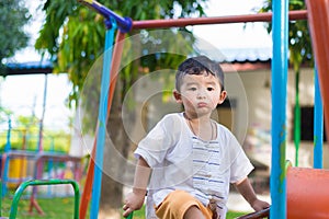 Young Asian boy play a iron train swinging at the playground under the sunlight in summer.