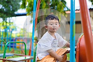 Young Asian boy play a iron train swinging at the playground under the sunlight in summer.