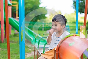 Young Asian boy play a iron train swinging at the playground under the sunlight in summer.